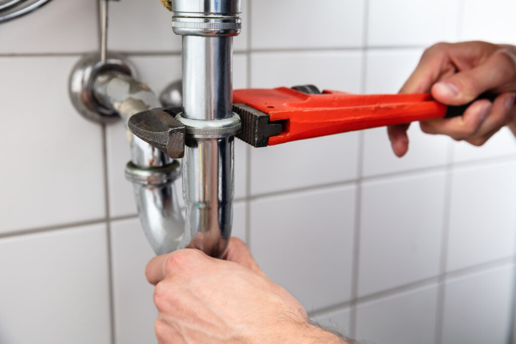 Close-up of a plumber’s hand repairing sink with adjustable wrench